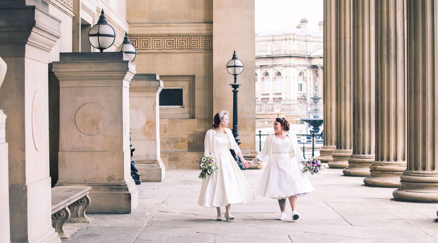 same sex wedding: 2 brides smile each other as they walk hand in hand outside St George's Hall