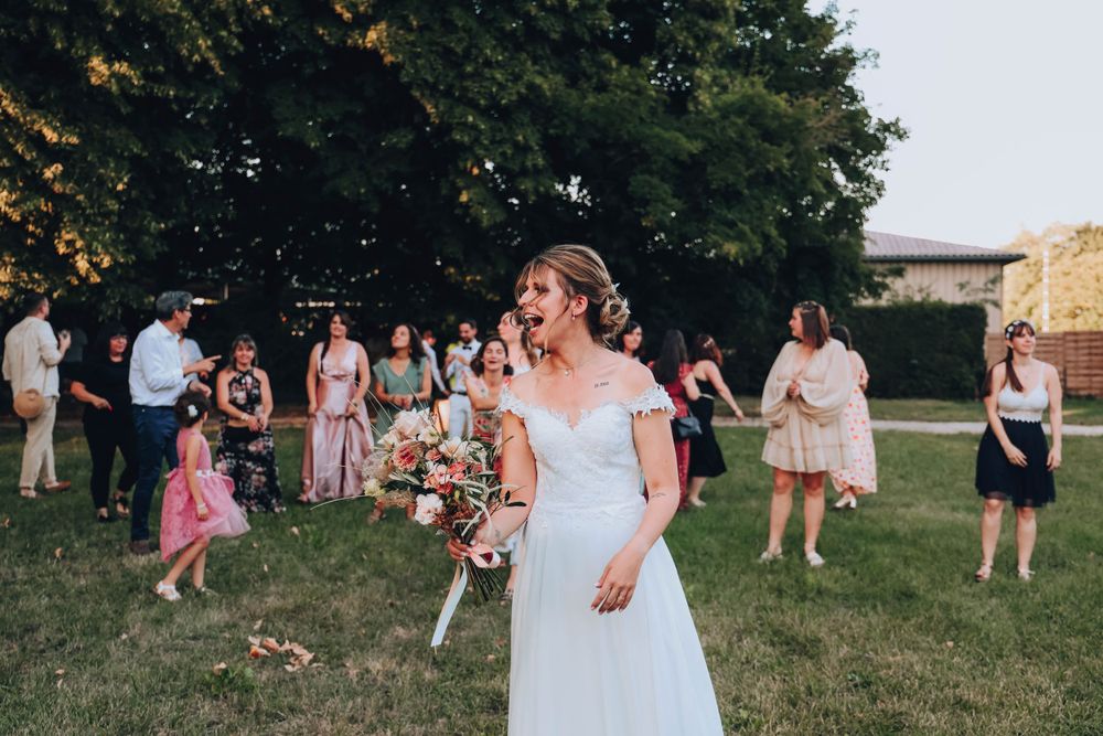 Bride in elegant white dress preparing to toss bouquet at outdoor reception.