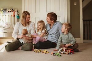 Family members gather on a hardwood floor playing with toys and enjoying quality time together.