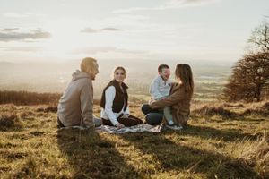 Family enjoying a sunset picnic on a grassy hilltop with scenic views.