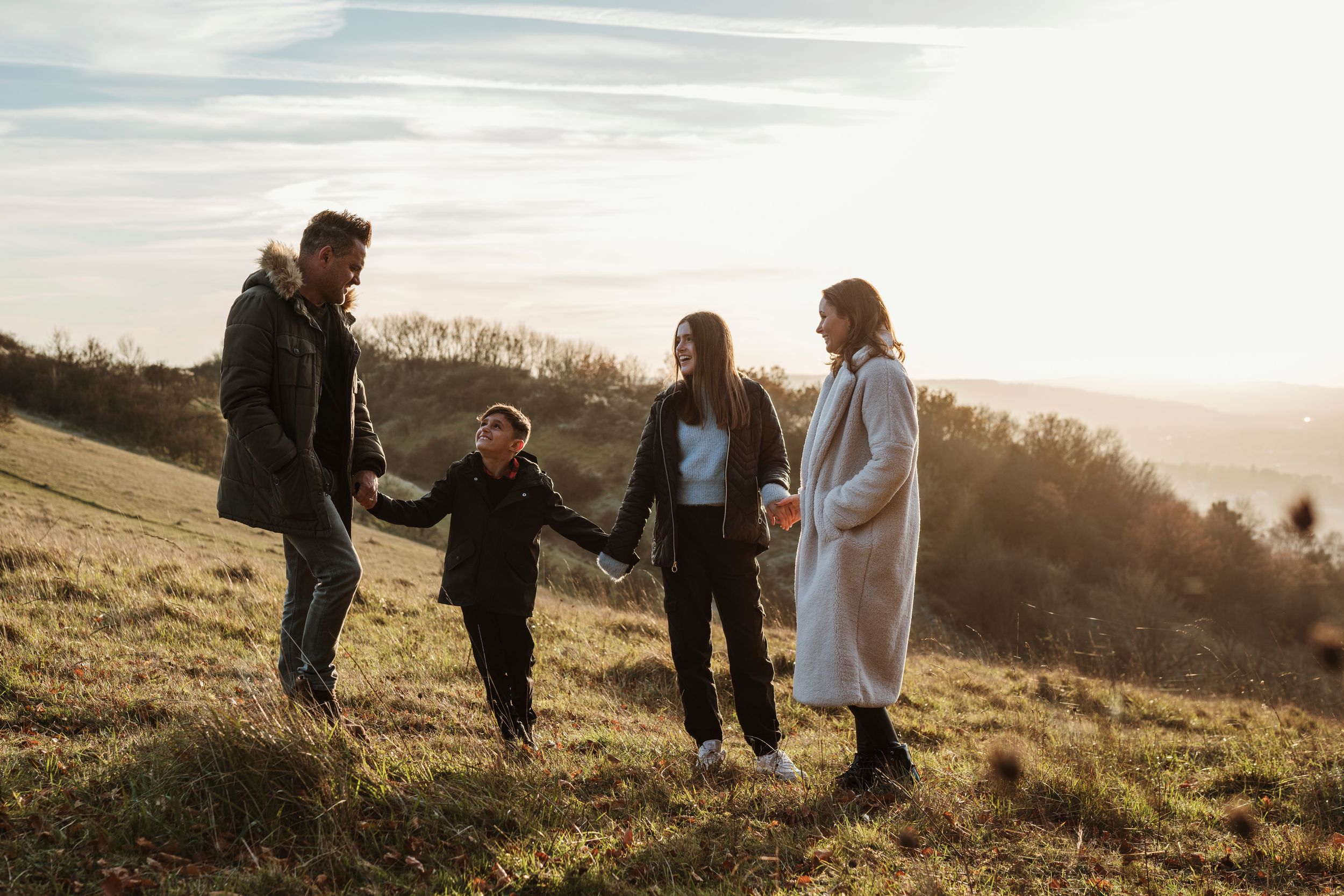 Family walking together on a grassy hillside during golden hour sunset.