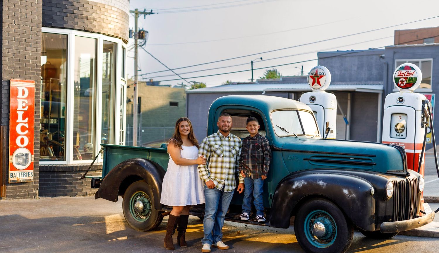 Vintage blue pickup truck parked outside a retro gas station with Pepsi signage visible.