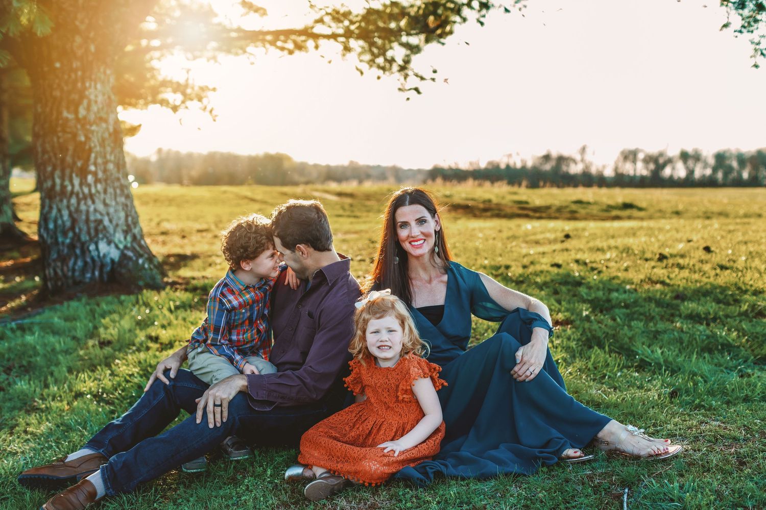 Family sitting together under a large tree during golden hour in autumn.