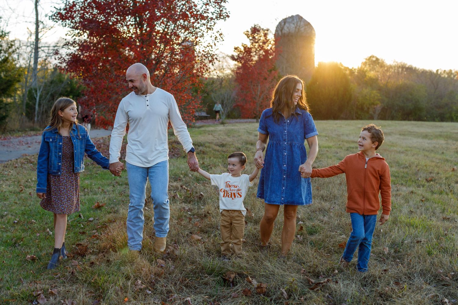 Family of five walking together in a field during golden hour sunset.