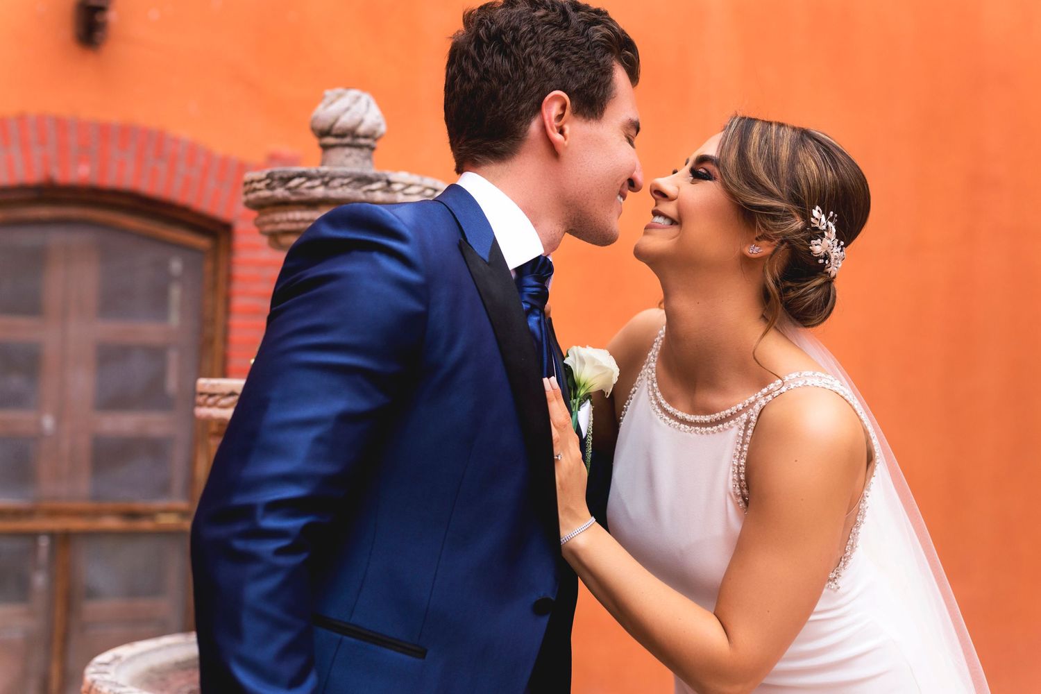 Wedding couple sharing a romantic moment against a bright orange wall background.