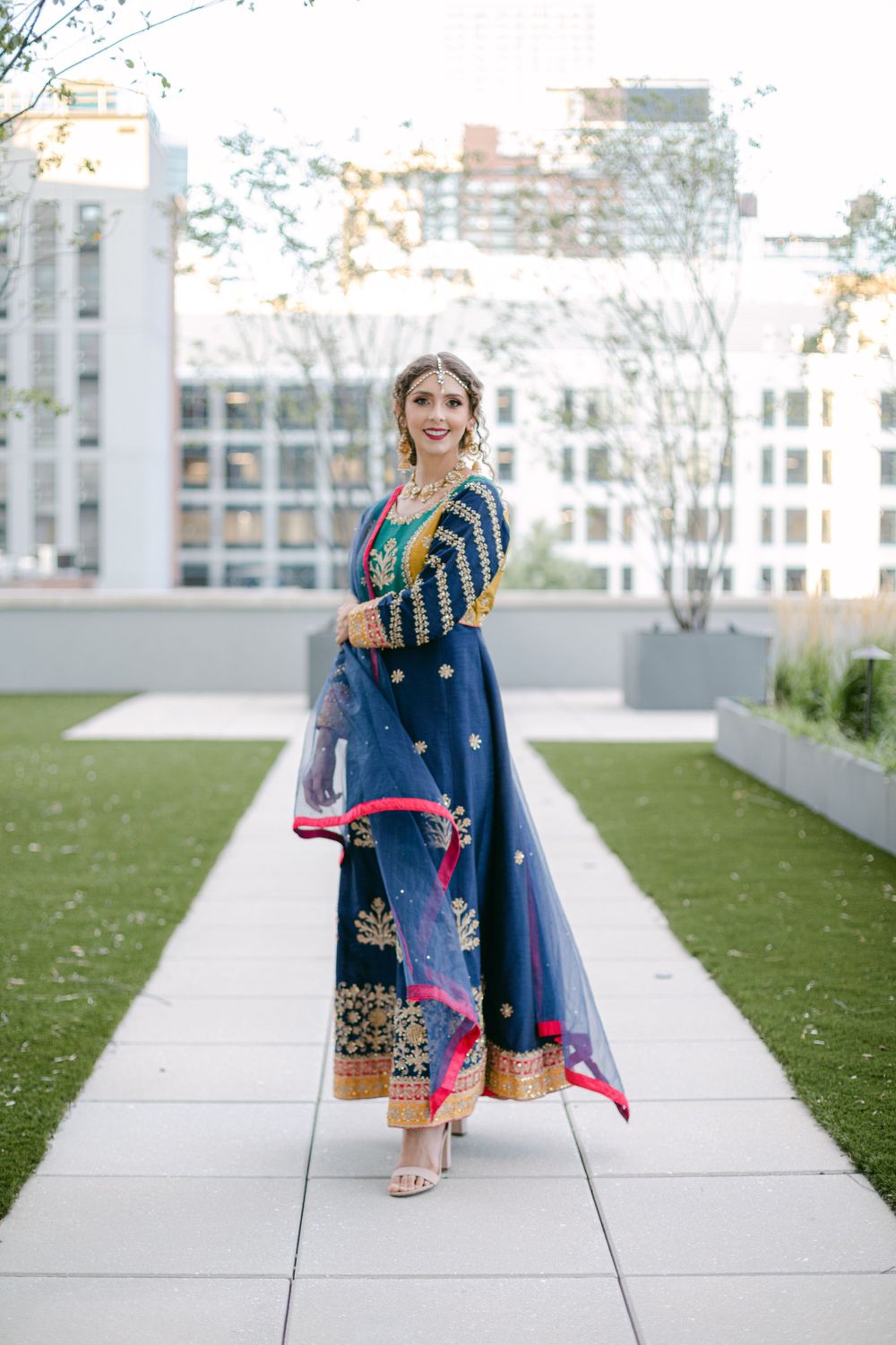 Full-length view of navy and gold traditional Indian ensemble on urban rooftop garden path.