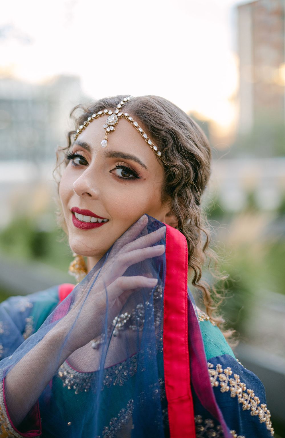 Close up portrait showing detailed headpiece and traditional South Asian bridal makeup at sunset.