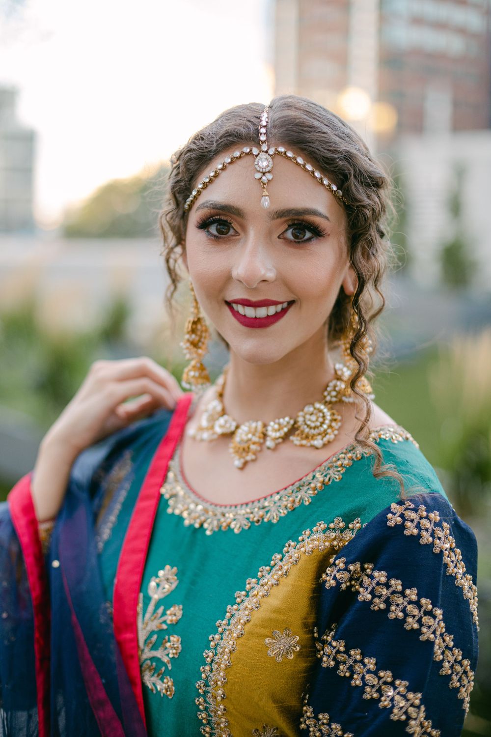 Detailed shot of traditional Indian bridal jewelry and emerald green and navy outfit with gold accents.