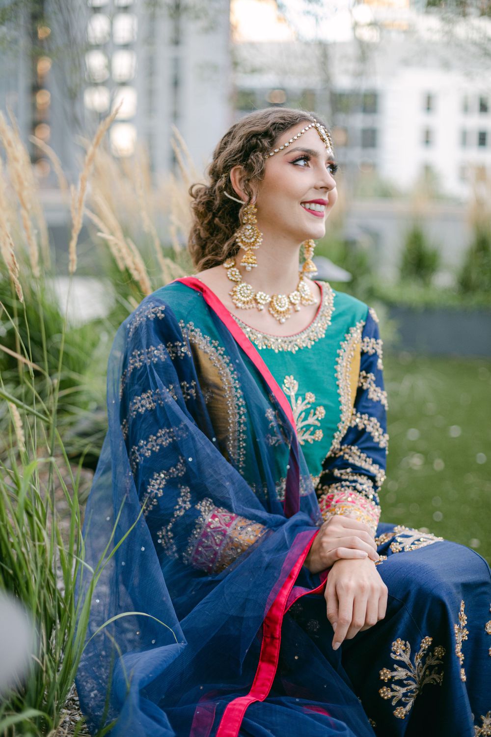 Traditional South Asian outfit in navy and emerald with gold embellishments photographed among tall grasses.