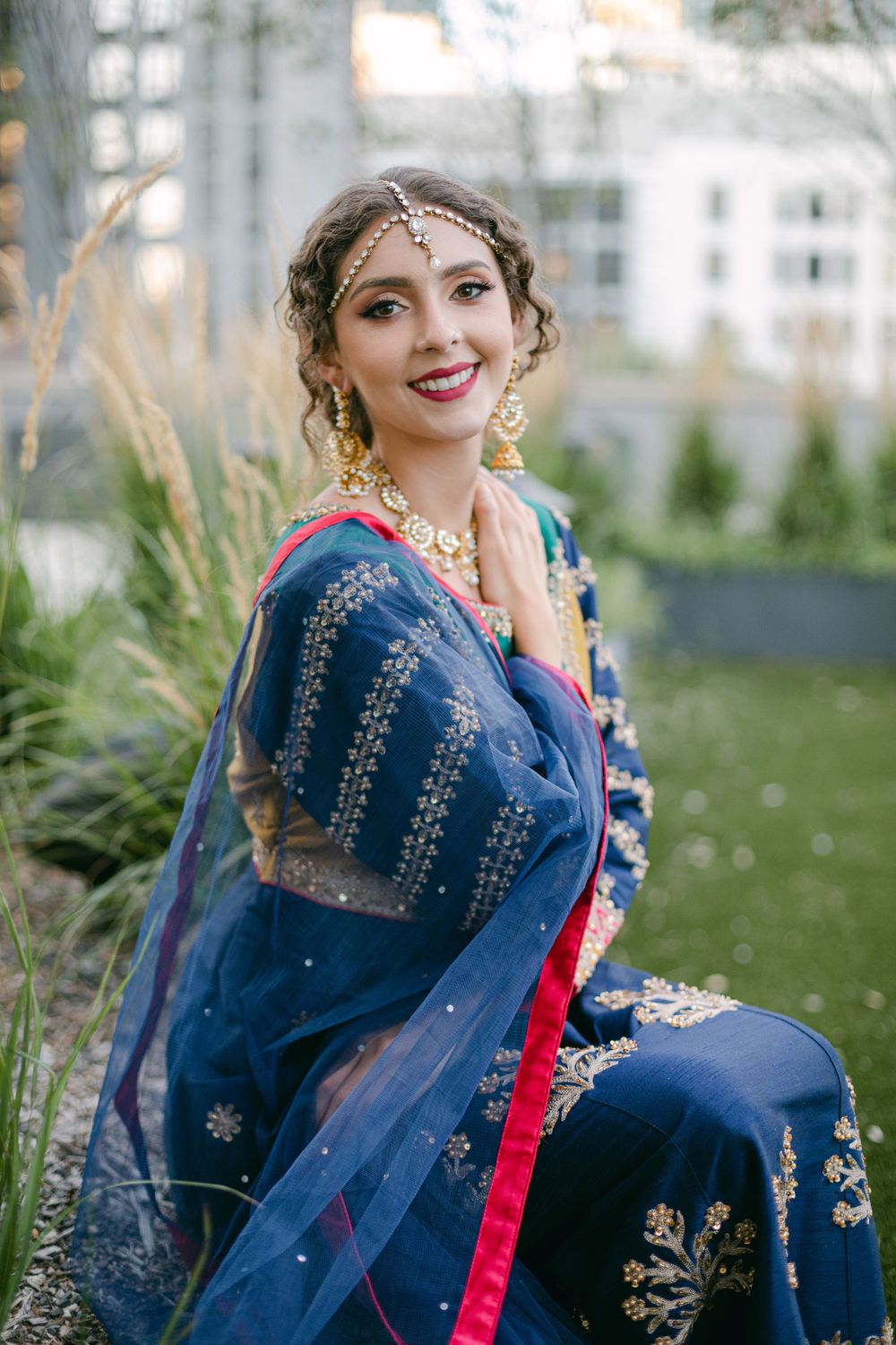 Traditional South Asian bridal attire featuring navy blue embroidered lehenga with red trim in outdoor garden setting.