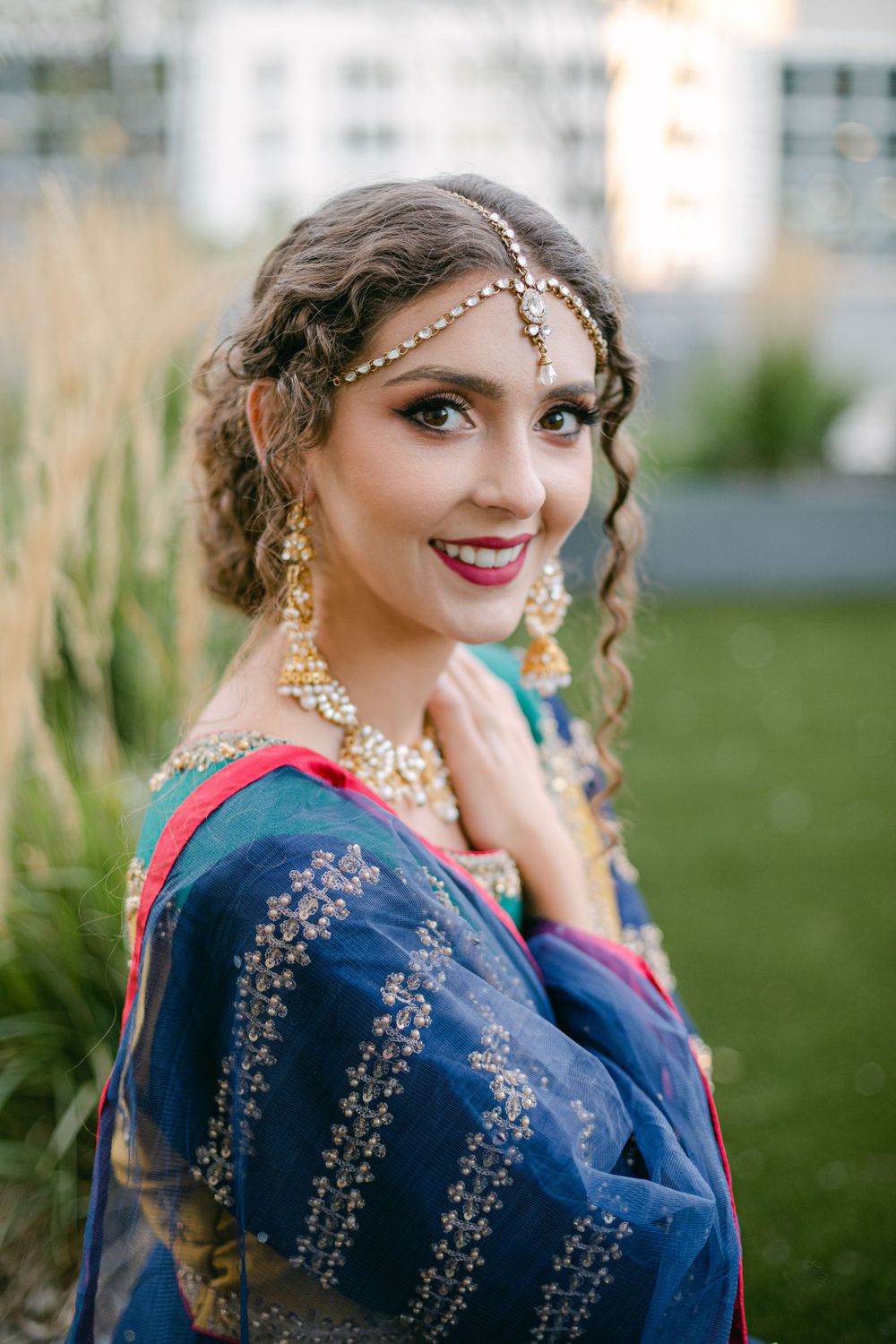 Close-up of ornate bridal jewelry and navy embroidered outfit against garden backdrop.