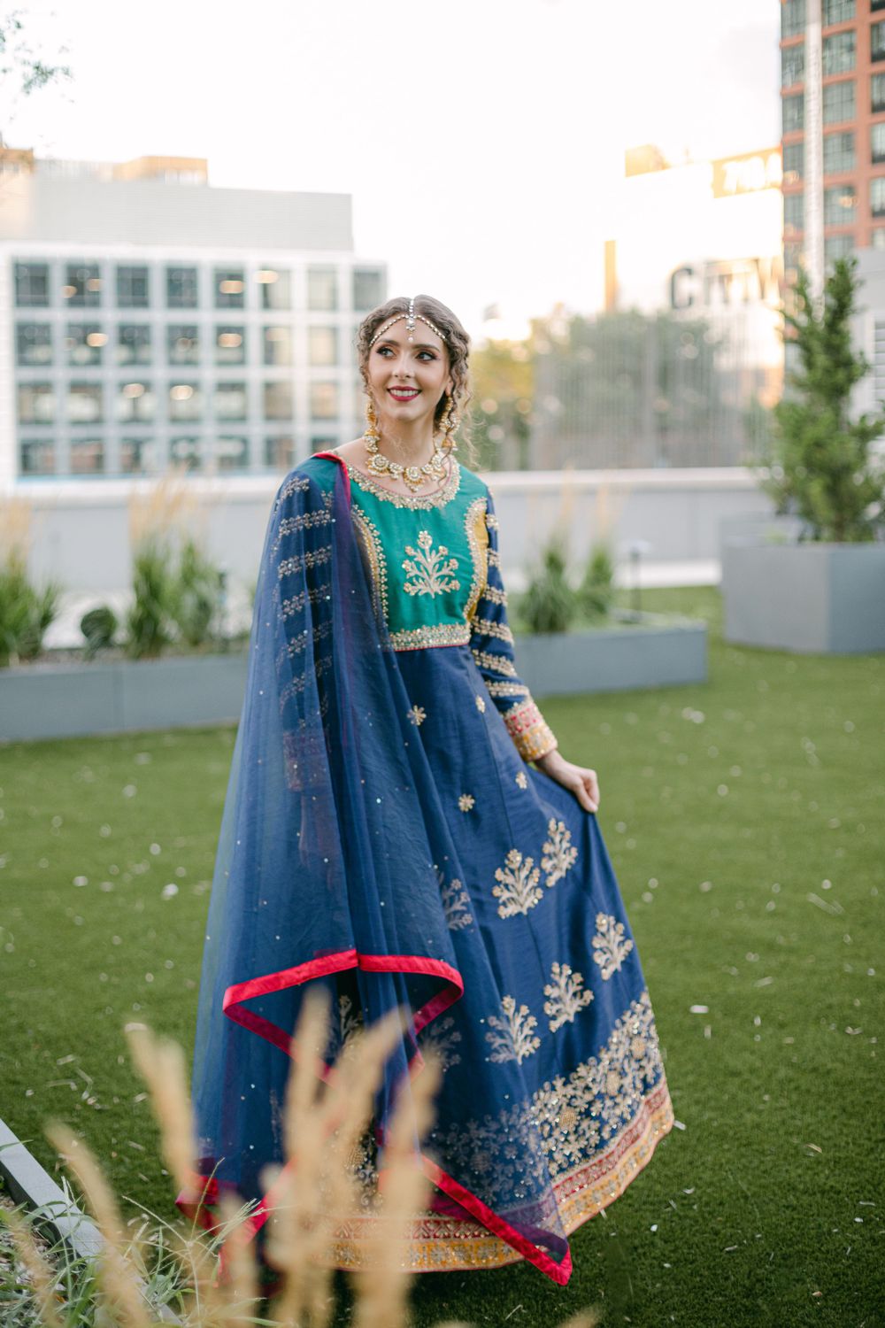 Elegant navy blue and turquoise lehenga with intricate embroidery photographed in urban rooftop garden.