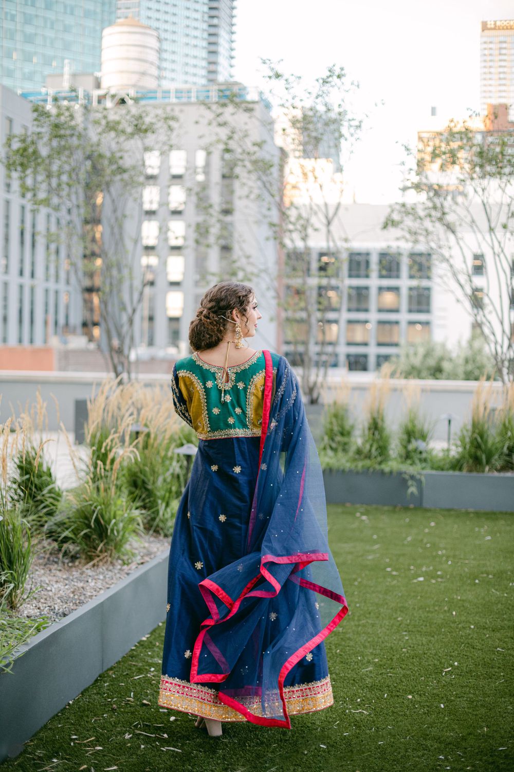 Back view of navy blue lehenga with pink border trim against urban cityscape.