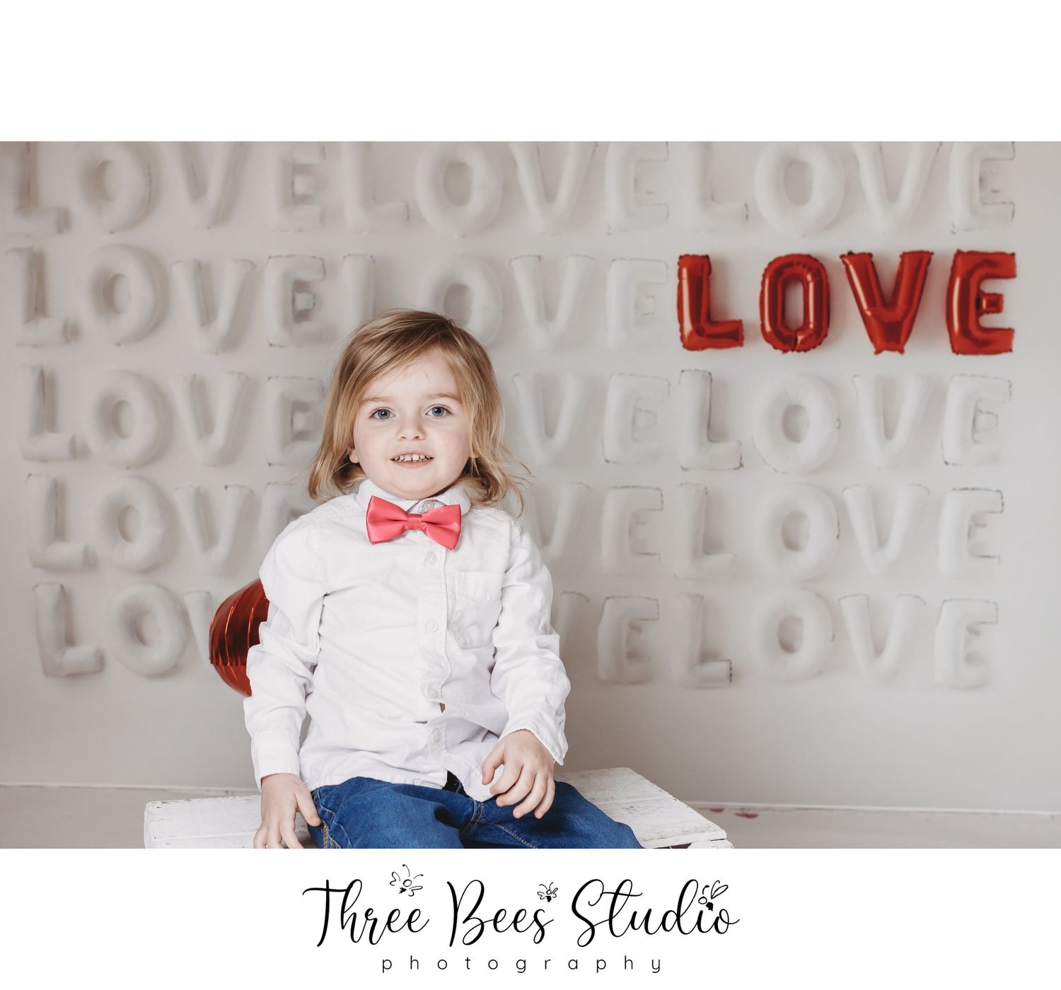 Studio portrait with love backdrop featuring child in white shirt and red bowtie.
