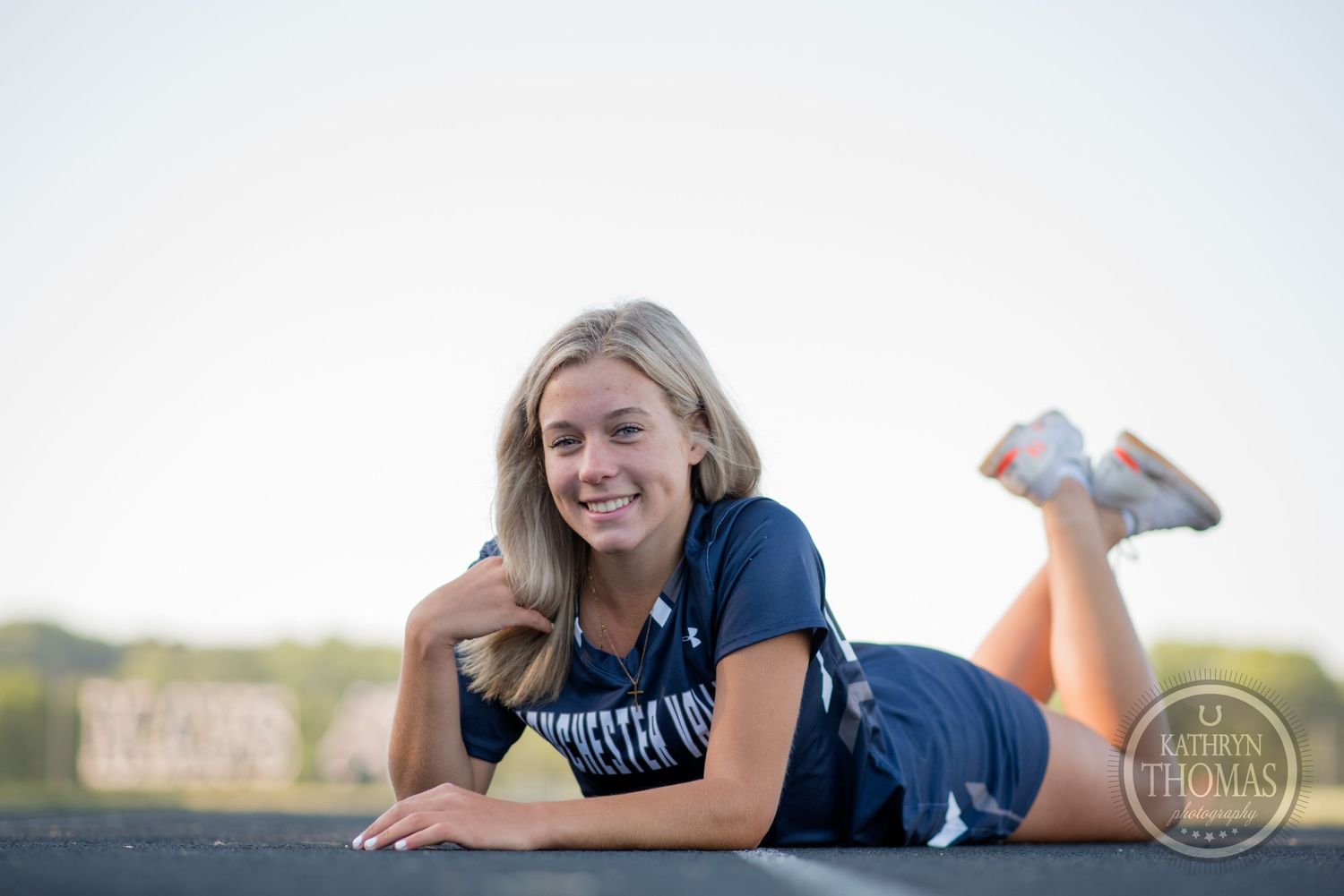Student athlete in navy blue uniform lounges on track surface during outdoor sports photoshoot.