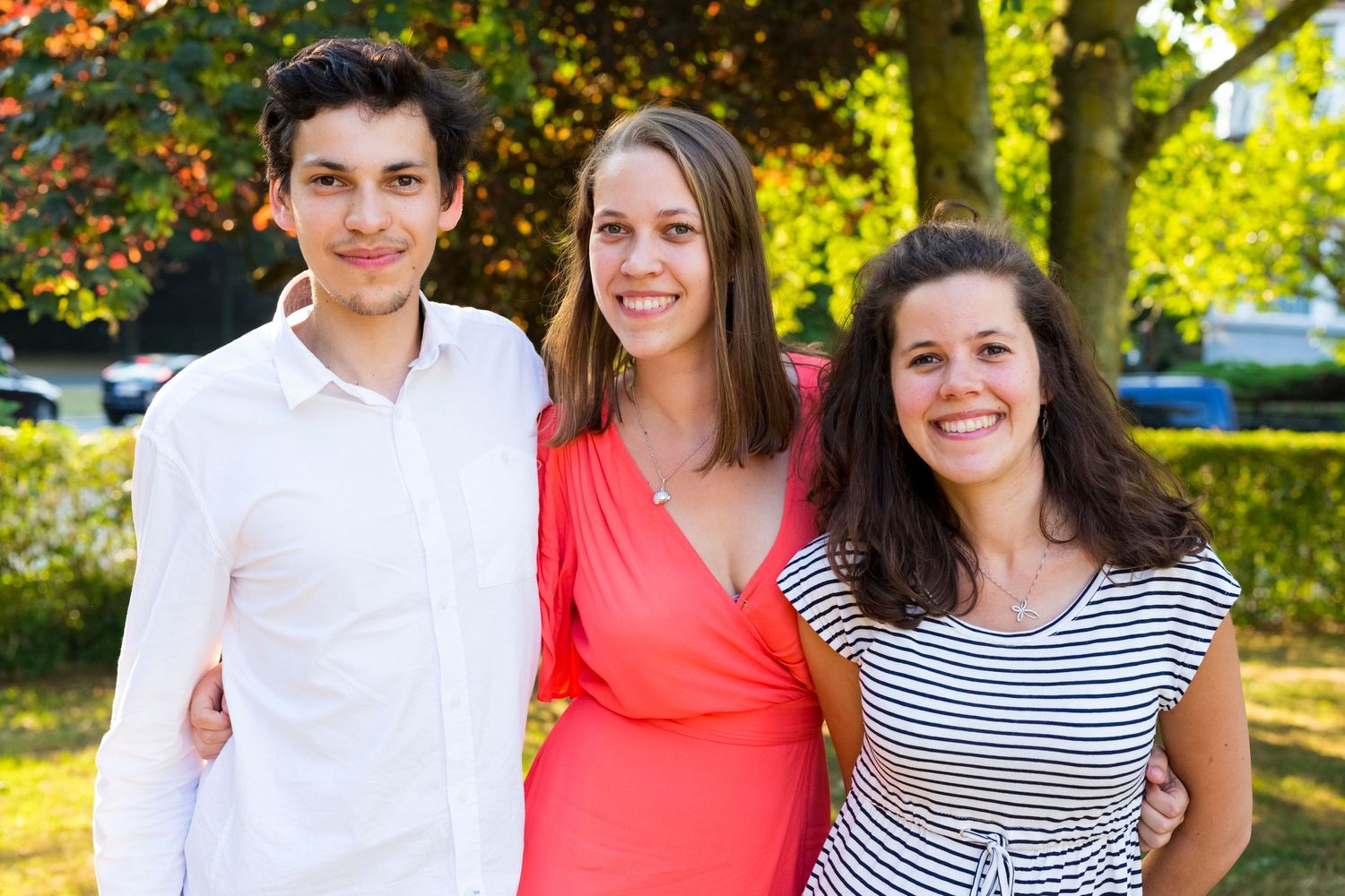 Three friends pose together on a sunny day with flowering trees in the background.