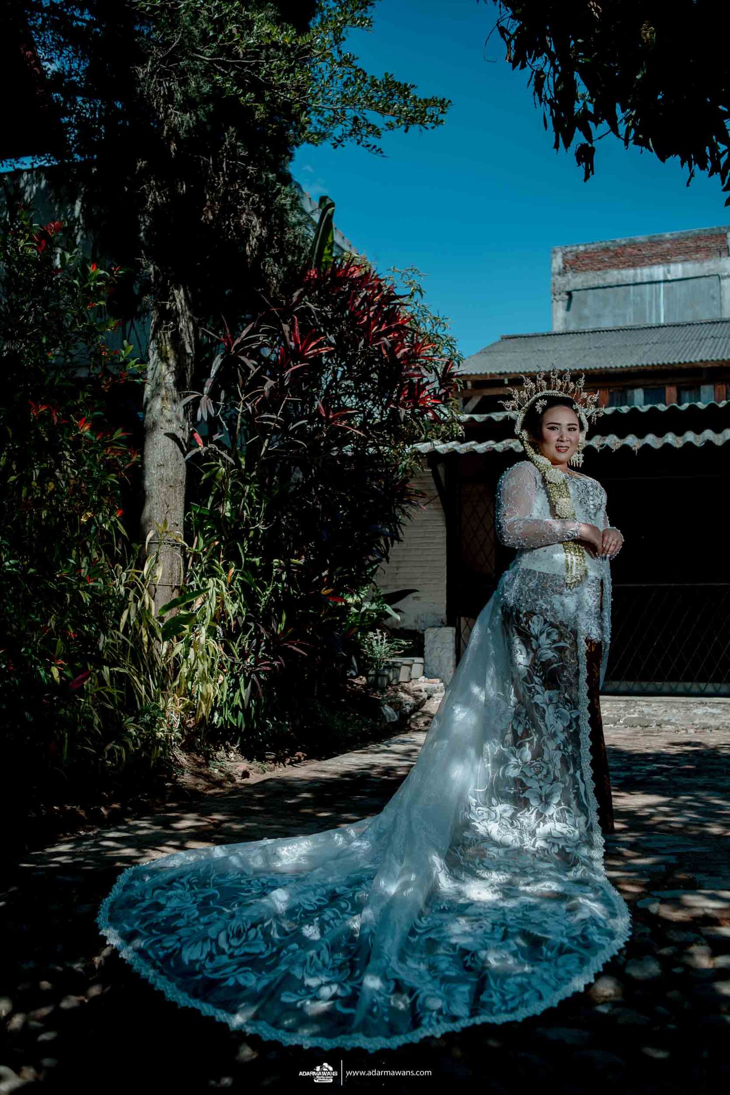 Dramatic outdoor bridal photo showing a long blue train dress against lush garden landscaping.