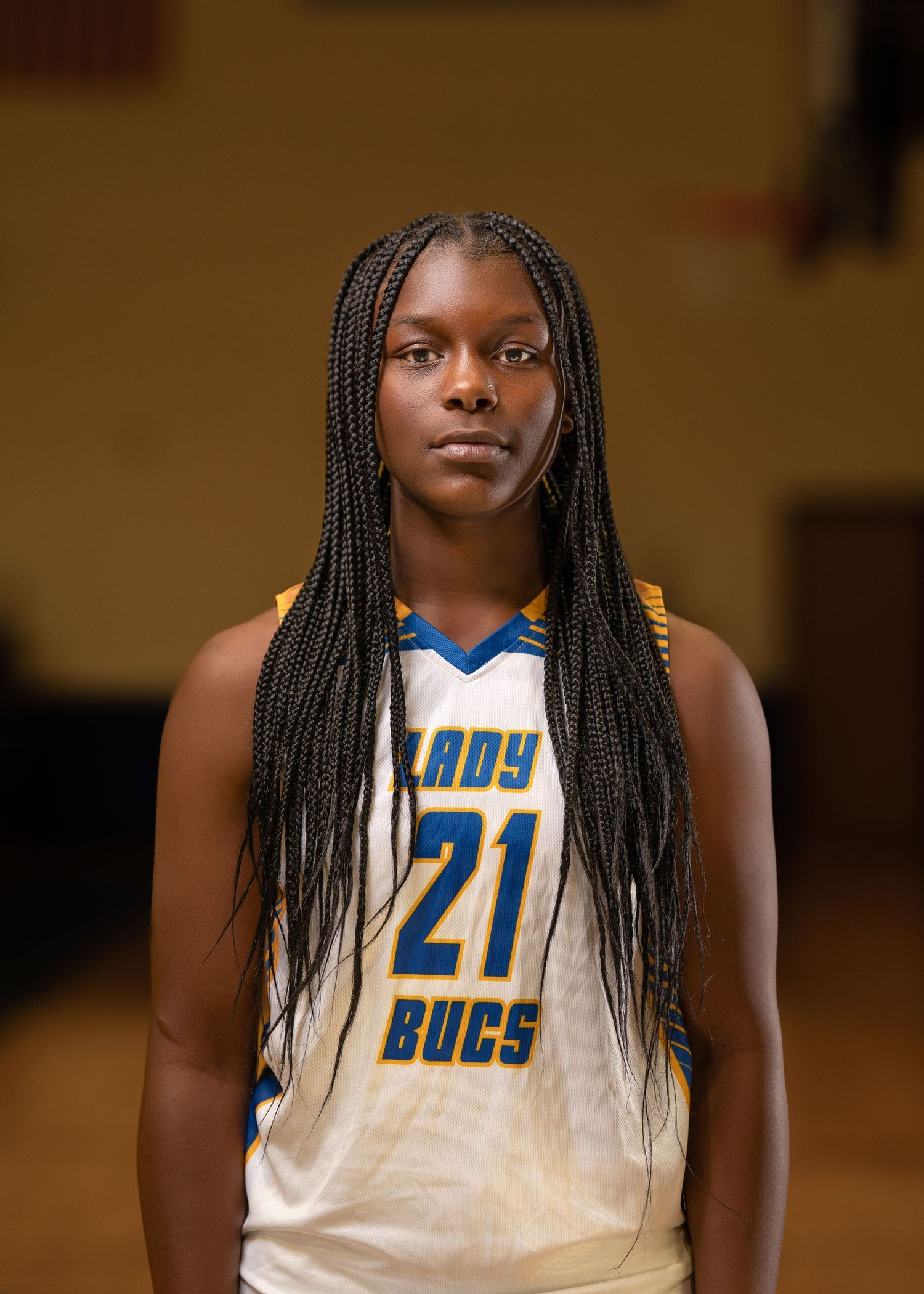 Basketball player with long braids wearing white Lady Bucs jersey number 21 poses for team photo.