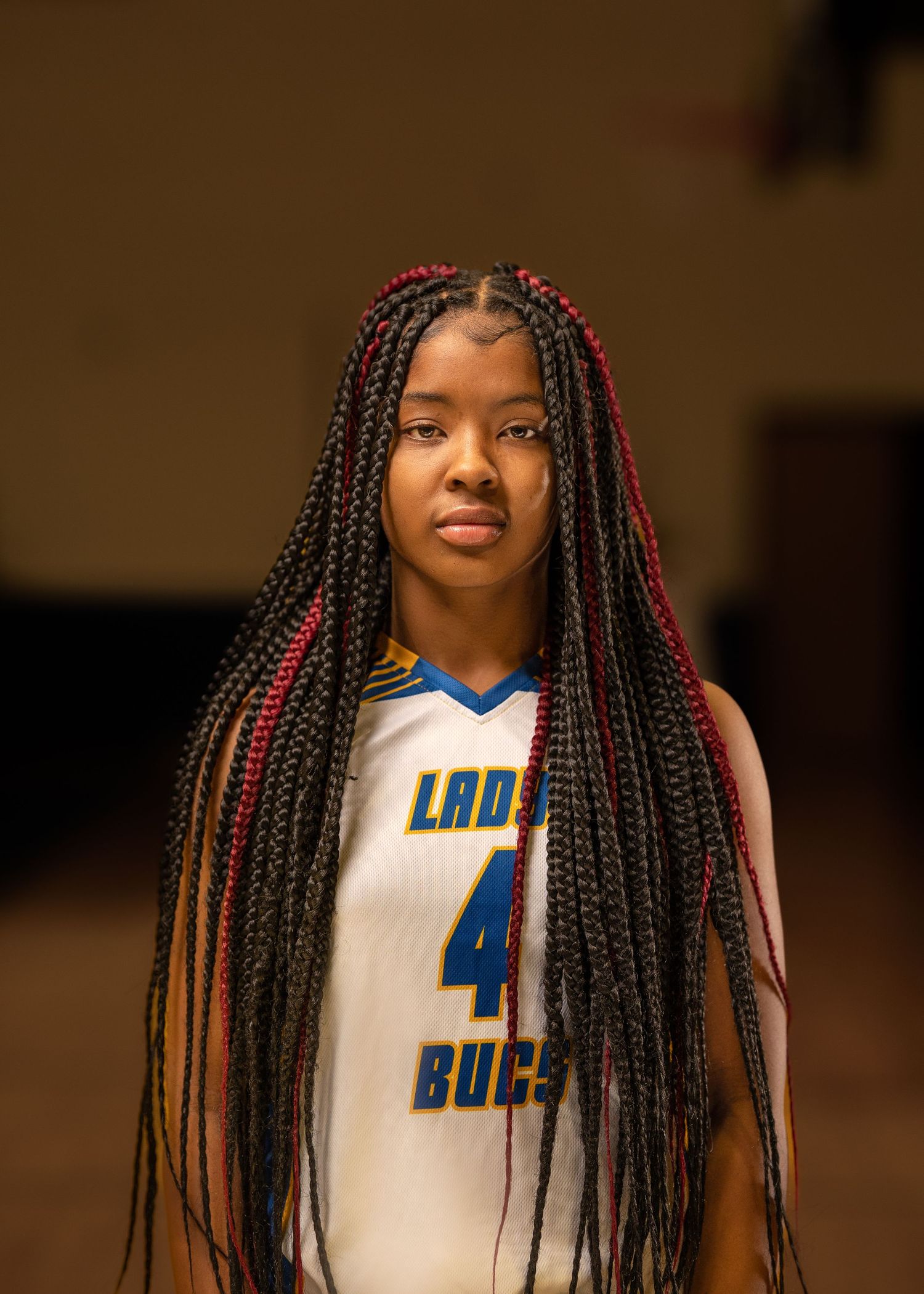 Basketball player with red-accented braids wearing Lady Bucs jersey number 4 poses for photo.