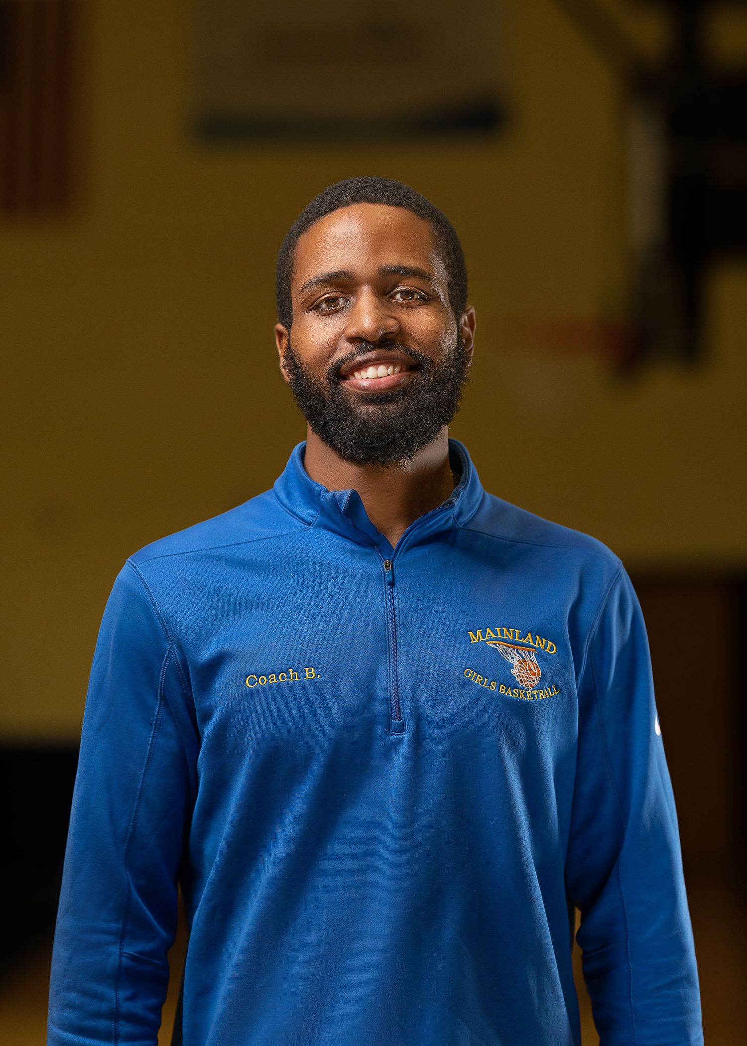 Coach wearing blue Mainland quarter-zip pullover stands against warm background.