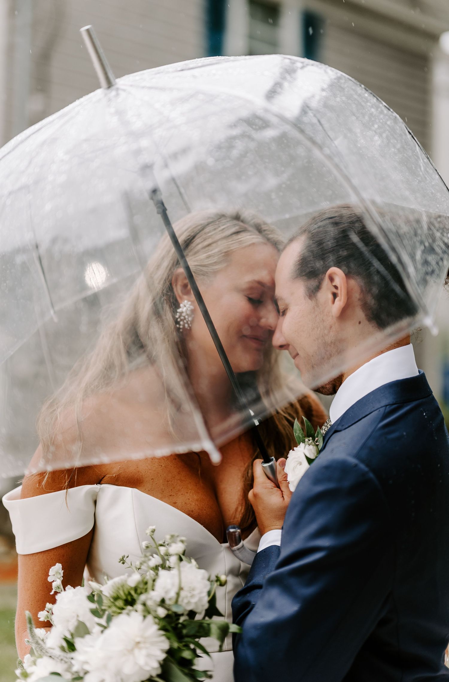 A romantic couple shares an intimate moment under a clear umbrella on their wedding day.