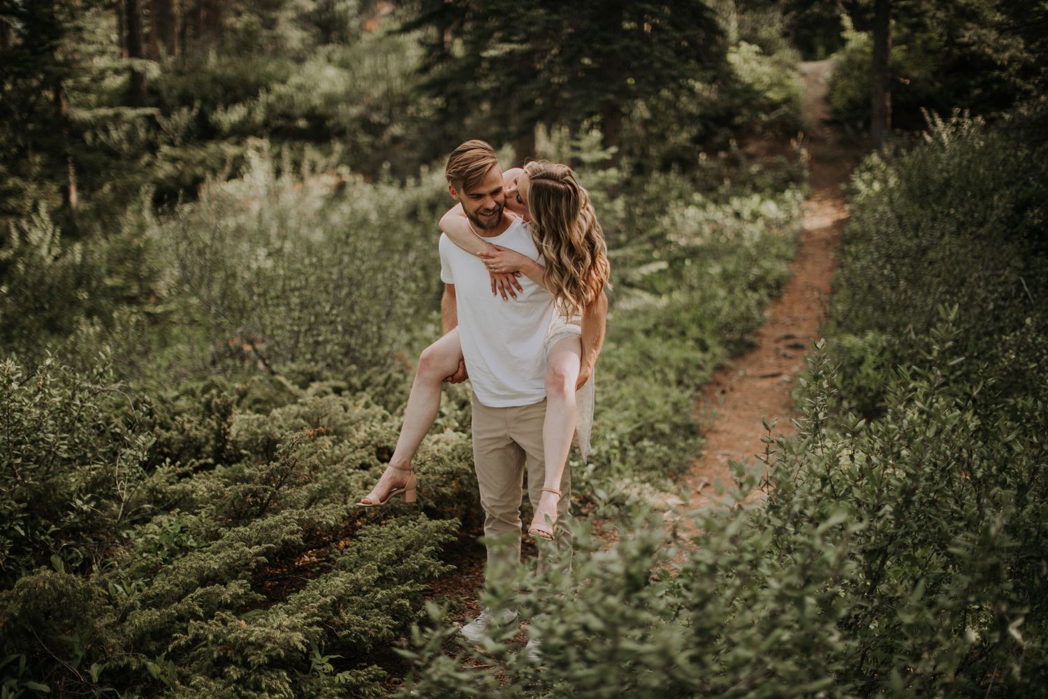 A couple shares an intimate moment on a forest trail during golden hour.