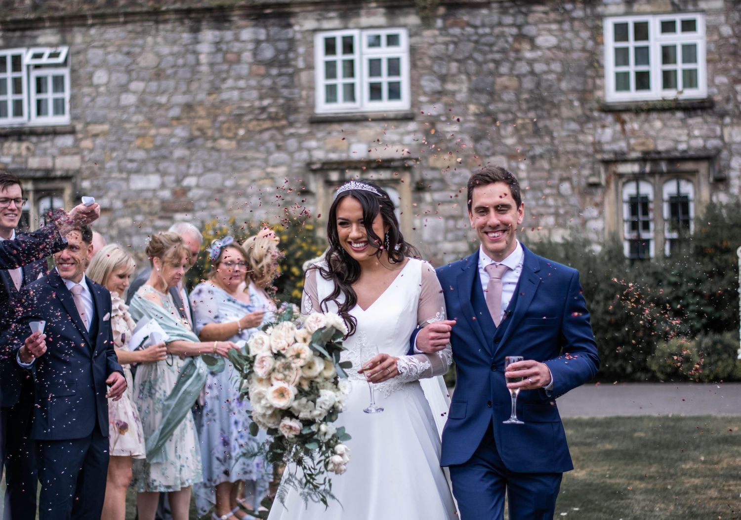 Wedding party celebrating with confetti outside historic stone building.