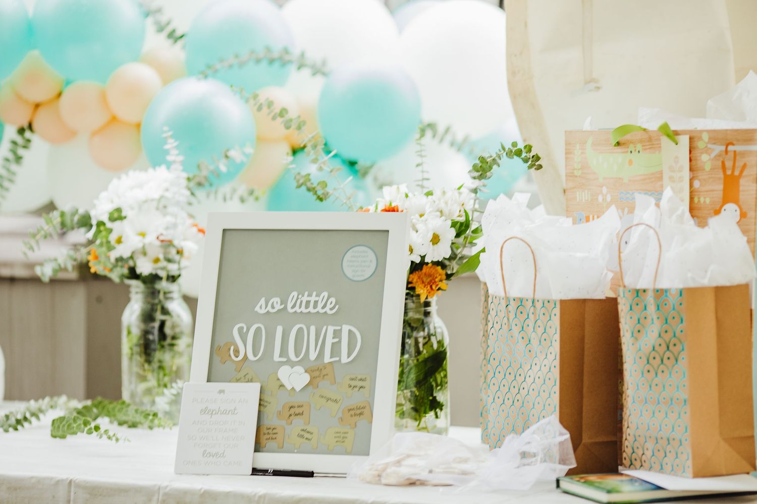 Baby shower decoration with balloons, gift bags and 'so little so loved' sign.