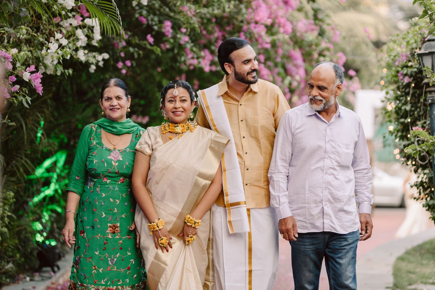 Family group wearing coordinated traditional attire stands together in an outdoor garden setting.