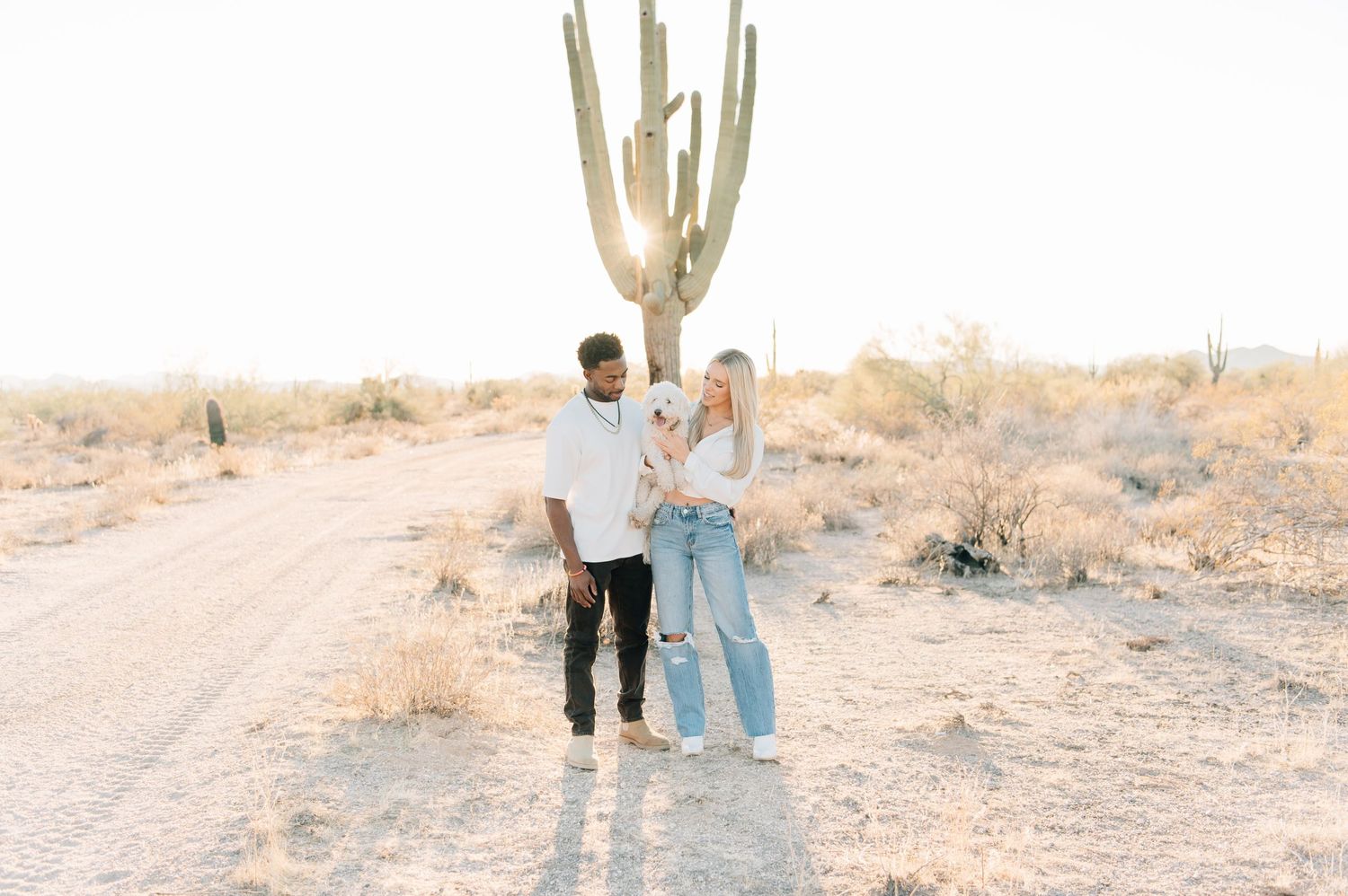Couple standing together in desert landscape near tall saguaro cactus during golden hour sunset in Arizona.