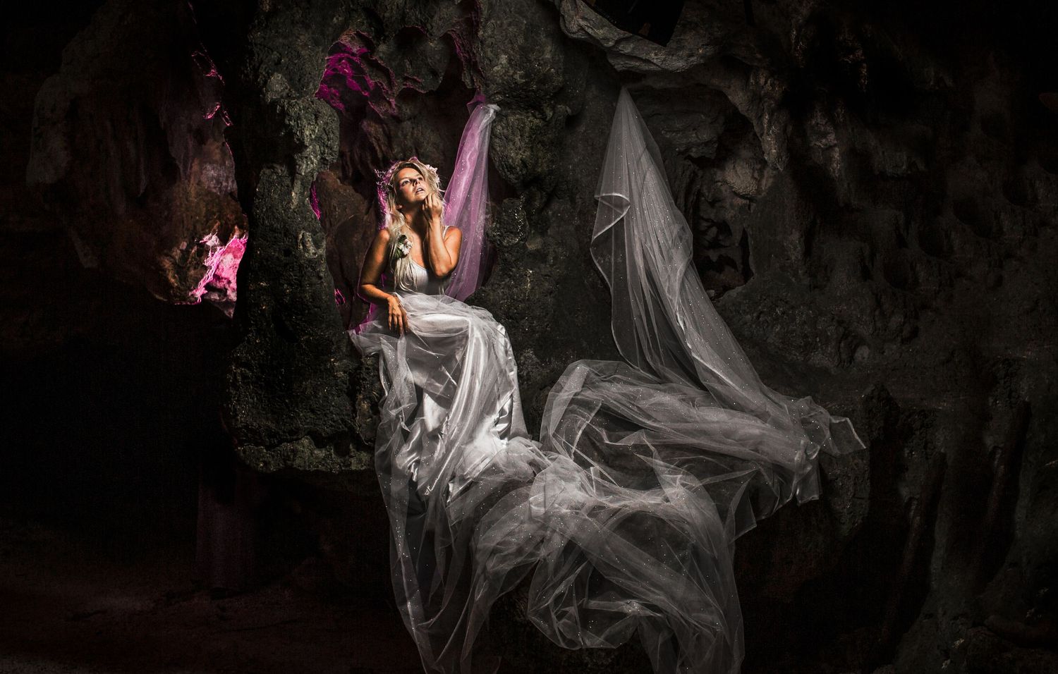 Ethereal photoshoot in a dark cave with flowing white fabric and dramatic lighting.