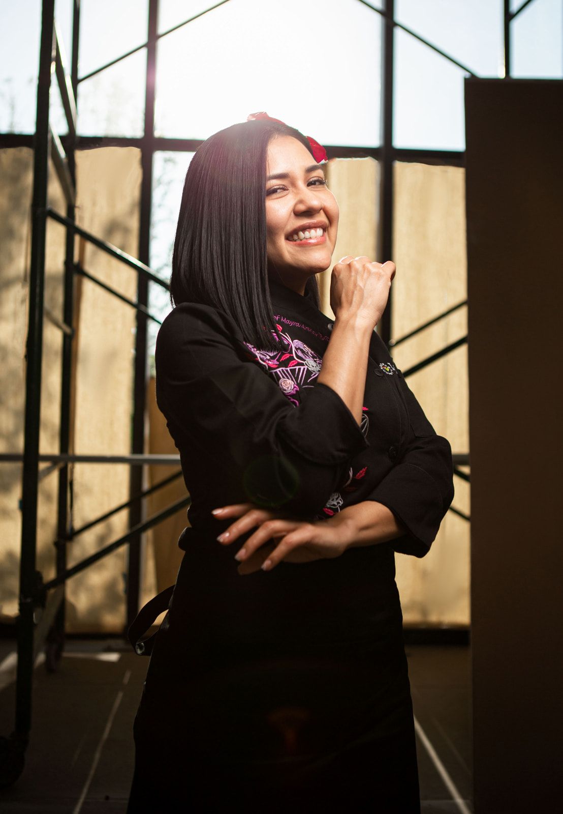 Portrait in black attire with embroidered details in warm backlit setting.