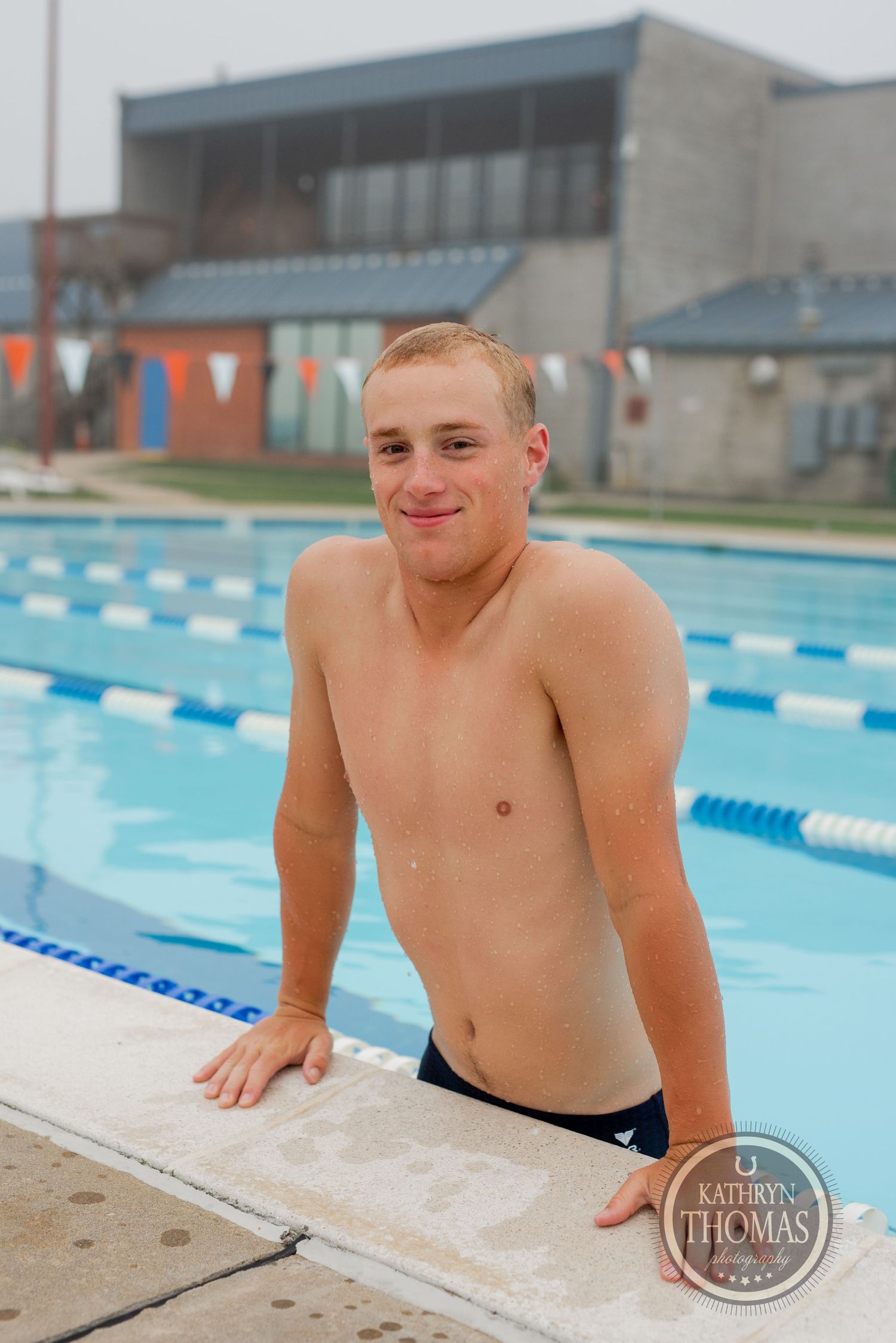A swimmer poses at the edge of a lap pool with orange and black pennant flags overhead.