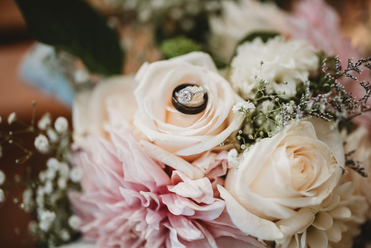 Close-up of blush roses and pink flowers in wedding bouquet with ring detail.