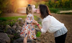 a mom kisses her young daughter on the cheek during their family photoshoot