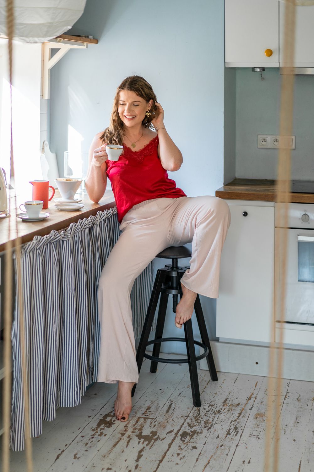 Person in red tank top and light pants sits casually on kitchen counter with coffee.
