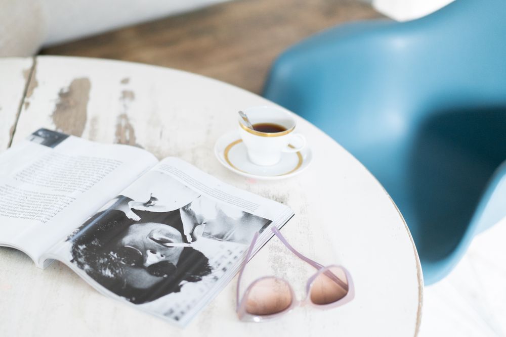 Lifestyle flatlay with coffee cup, magazine and sunglasses on white table.
