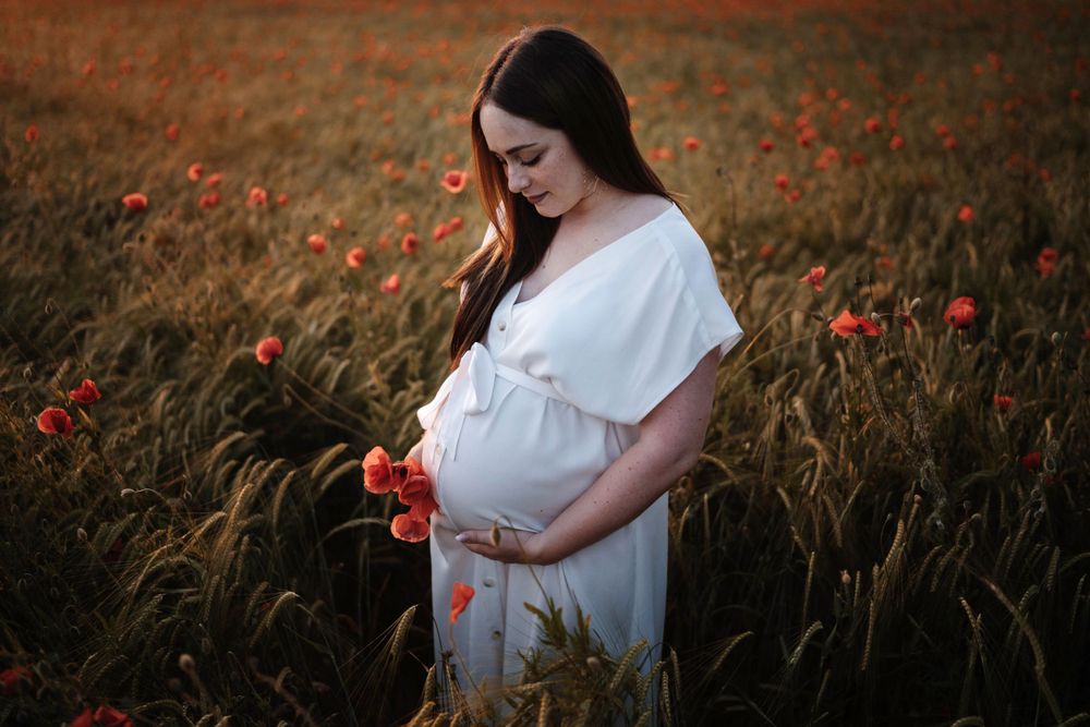 A person in a white dress stands in a golden wheat field dotted with vibrant red poppies at sunset.