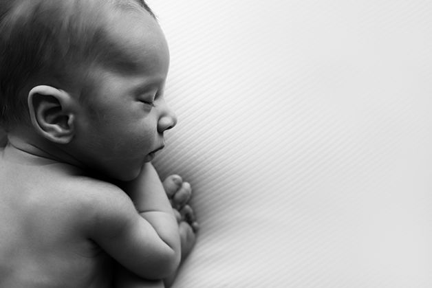 Side profile of newborn baby sleeping on white background.