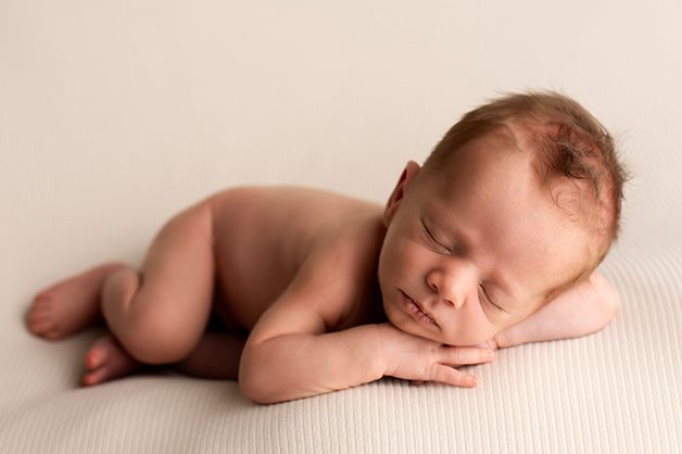 Peaceful newborn sleeping on ribbed cream fabric in warm-toned portrait.