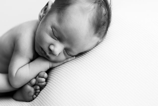 A black and white image of a sleeping newborn baby resting on a textured white surface.
