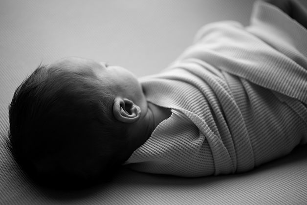 Black and white portrait of swaddled baby lying on side.