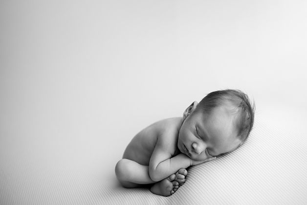 Peaceful sleeping newborn curled up on white background in black and white photography.