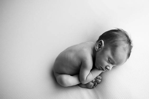 Sleeping newborn rests on textured white surface in monochrome portrait.