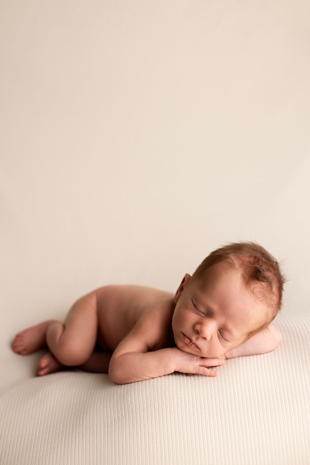 Sleeping newborn resting on cream textured background in artistic portrait.