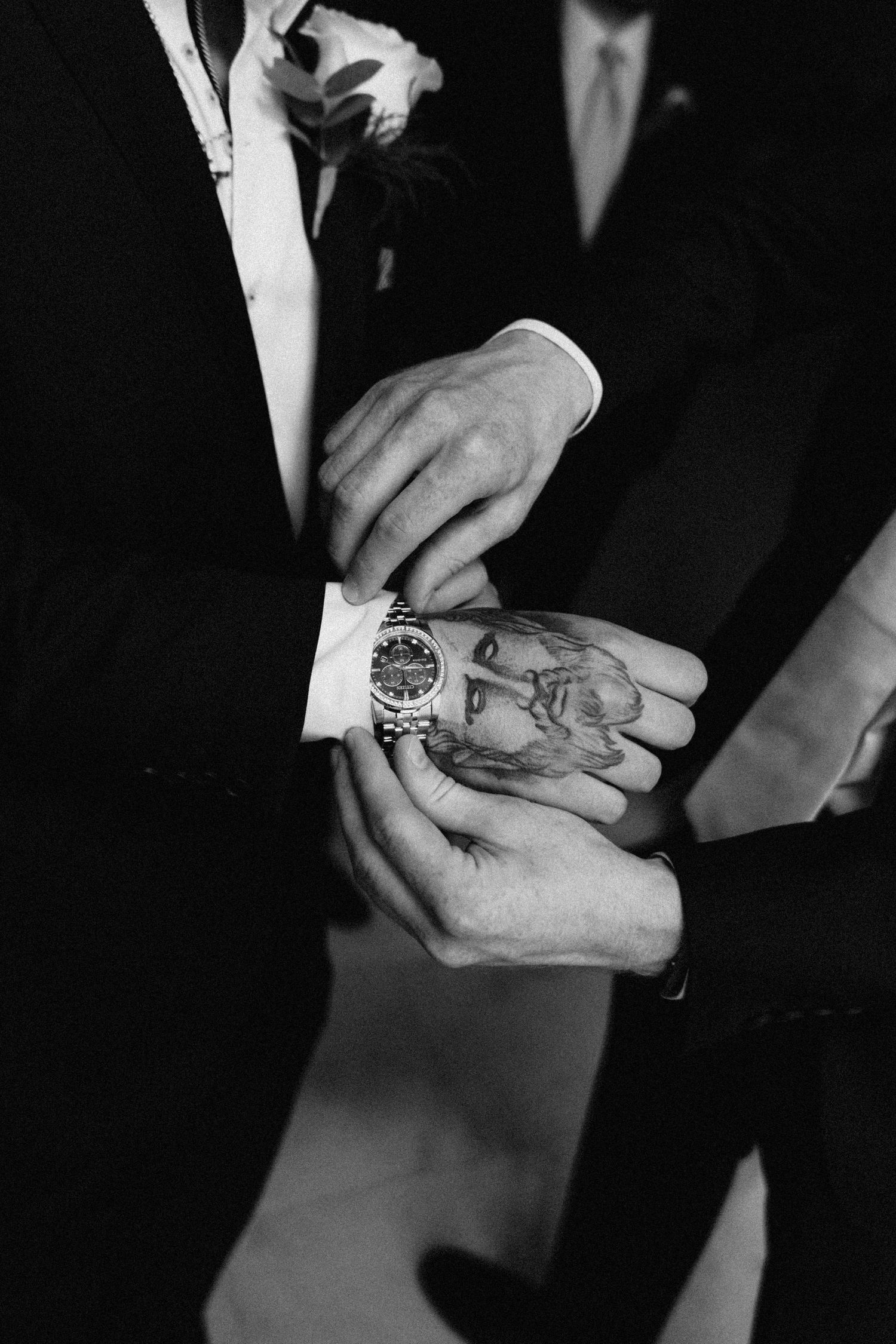 Black and white detail shot of watch and cufflink adjustment on formal suit sleeve.