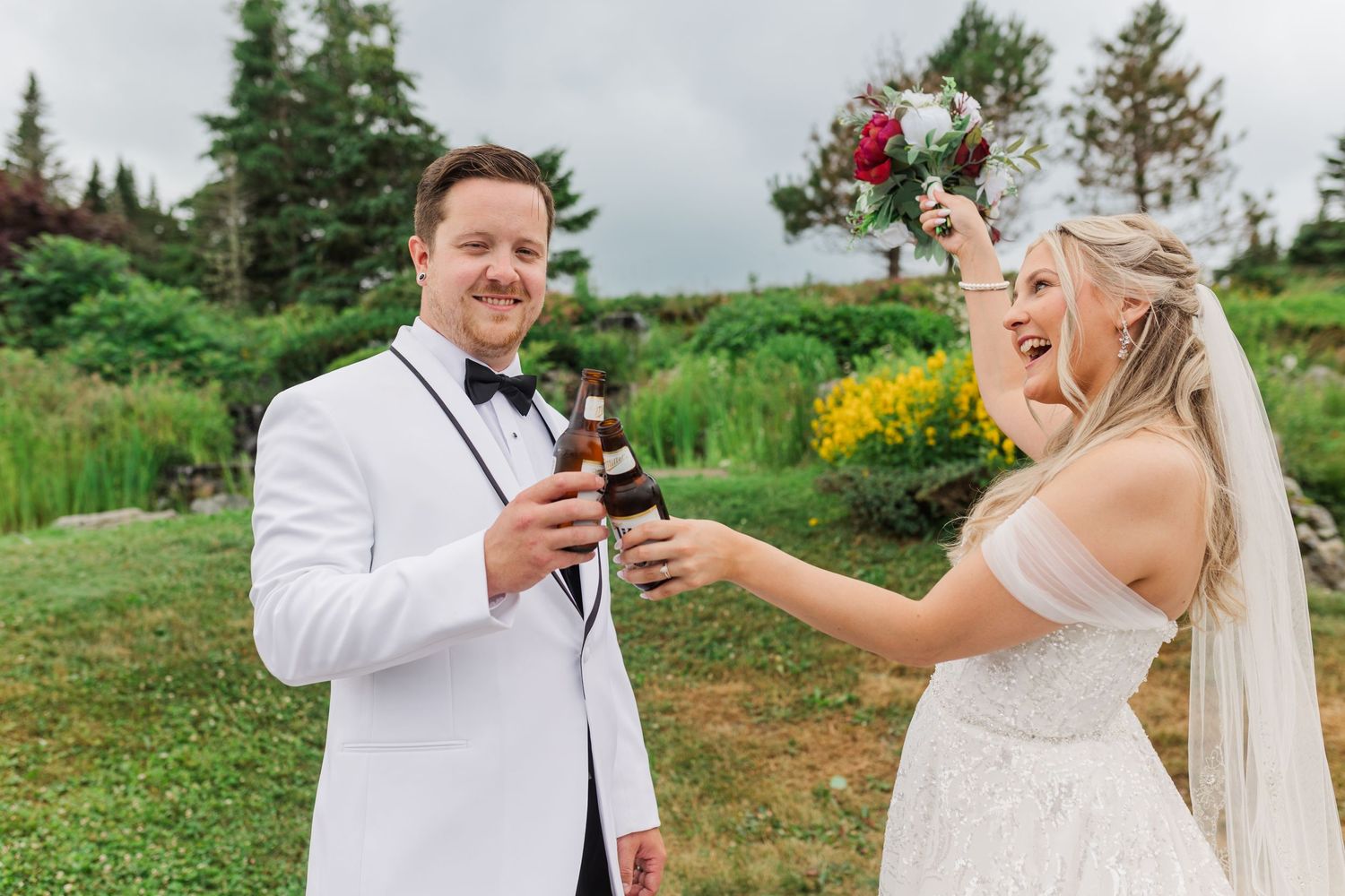 Couple shares a celebratory toast with wine glasses in front of greenery during outdoor garden wedding ceremony.