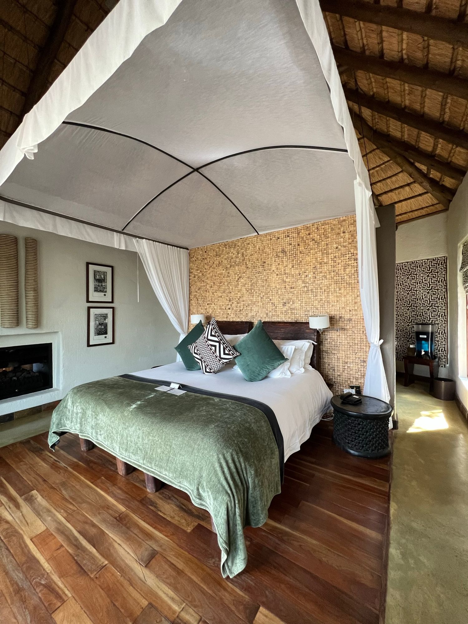Luxury safari lodge bedroom with canopy bed, hardwood floors and white drapes.