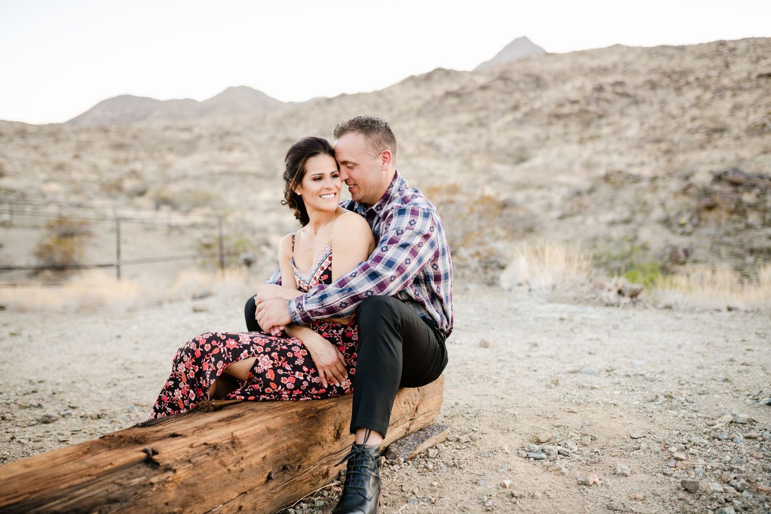 A couple sharing an intimate moment while sitting on a log in a desert landscape.