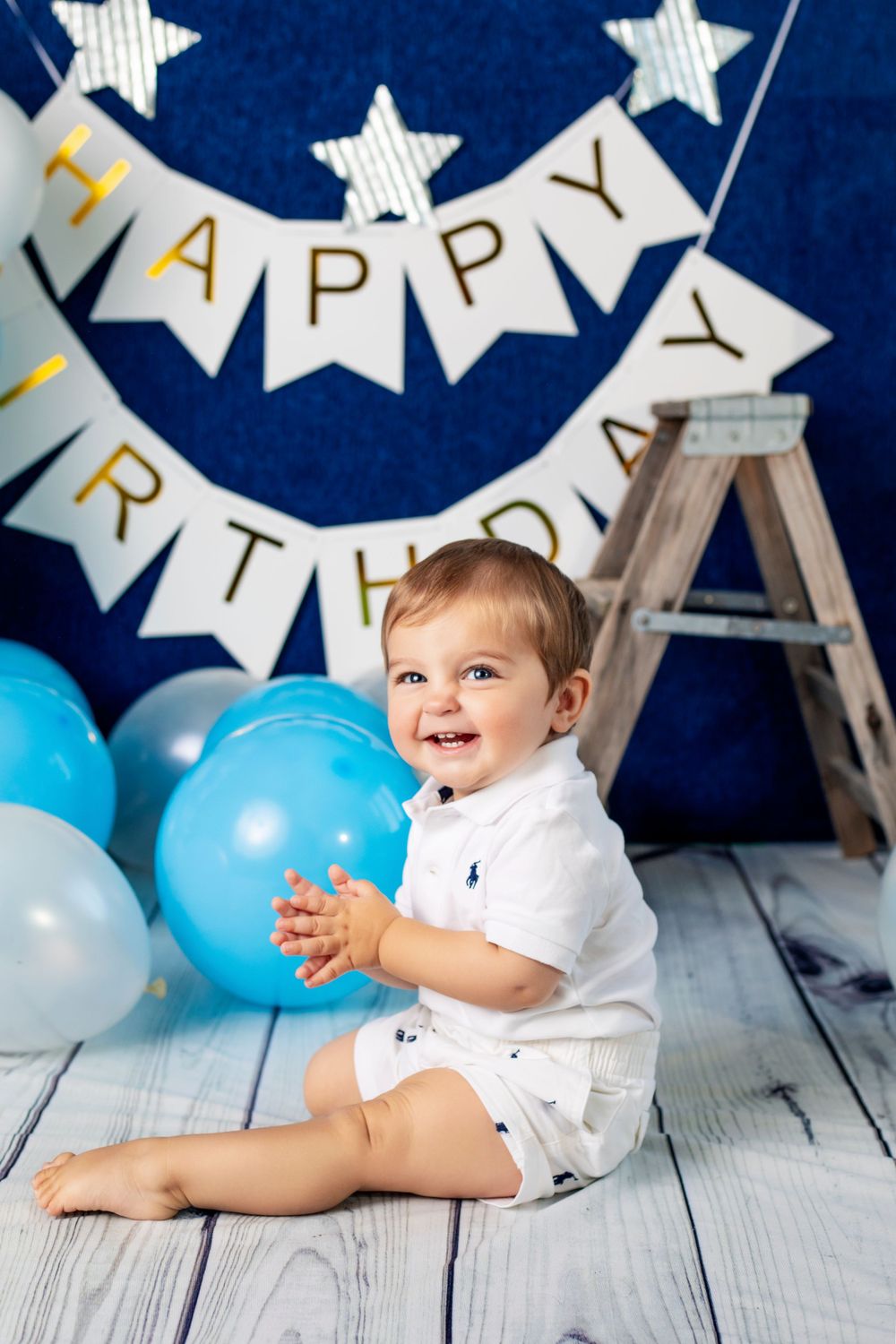 Birthday party scene with star decorations, blue balloons, and wooden ladder against navy backdrop.